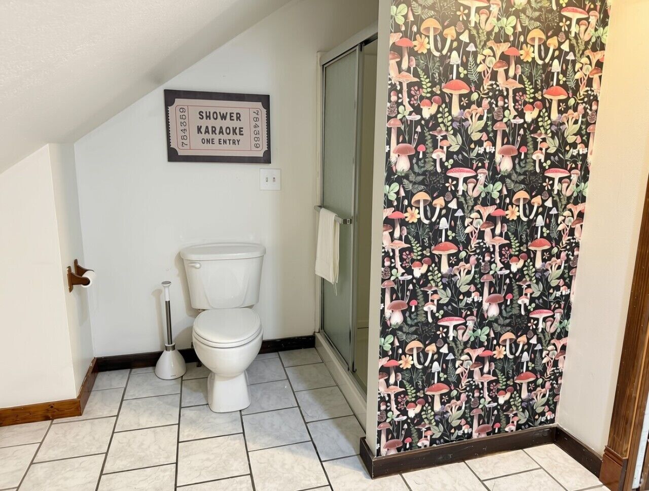 A bathroom with a toilet, a bidet, a shower sign, and a patterned shower curtain.