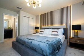 A modern bedroom with a large bed, bedside lamps, and a wall-mounted light fixture. - Luxury Disney Villa / 7BR with Themed Rooms & Private Pool in Windsor Island (Davenport)