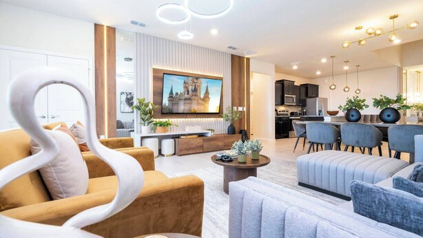 Una sala de estar moderna con un televisor grande, asientos cómodos y una cocina al fondo.