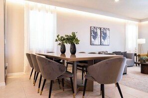 A modern dining area with a long table, grey upholstered chairs, and two vases with plants. - Luxury Disney Villa / 7BR with Themed Rooms & Private Pool in Windsor Island (Davenport)