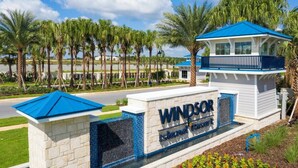 Letrero de 'Windsor Island Resort' con techo azul y paredes blancas, rodeado de palmeras y un cielo despejado.