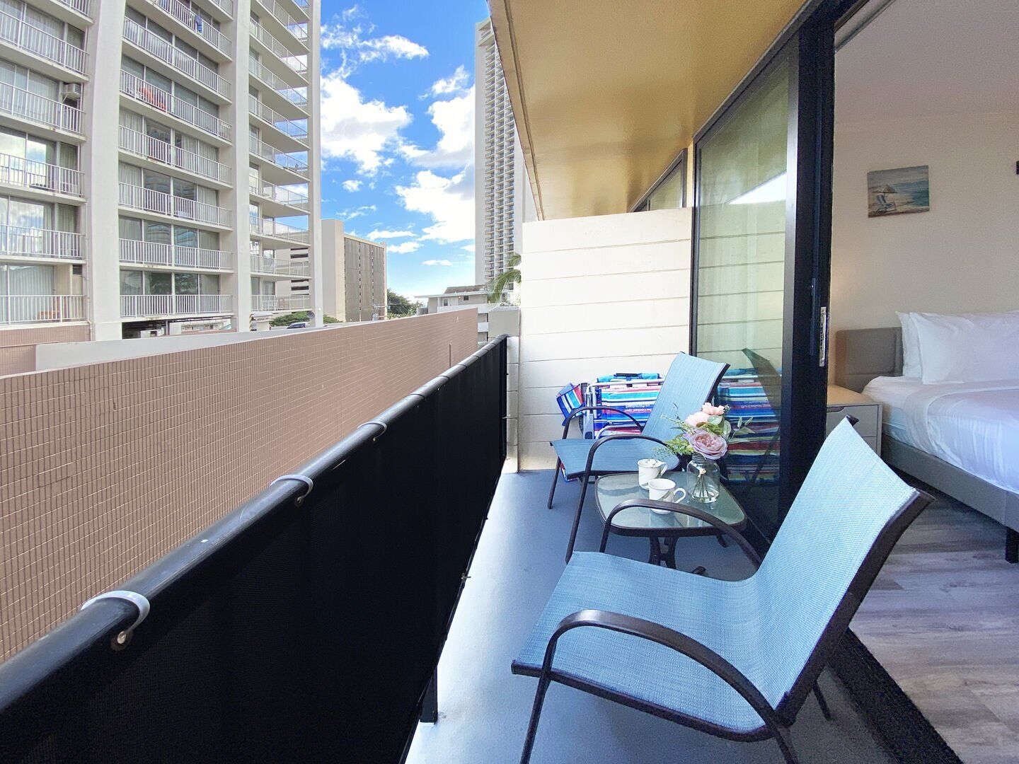 A balcony with a bed, a chair, and a table with books and a vase.