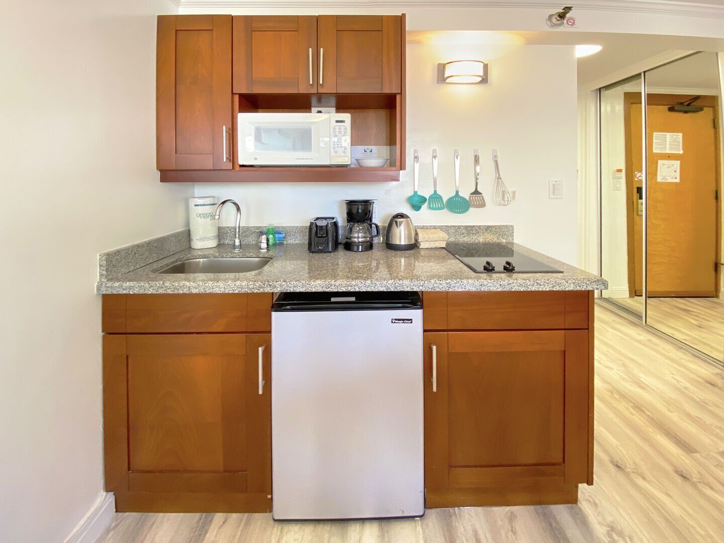 Una cocina compacta con armarios de madera, microondas integrado, lavavajillas y encimera de granito.