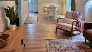 Una sala de estar moderna con comedor, piso de madera y un ventanal grande.