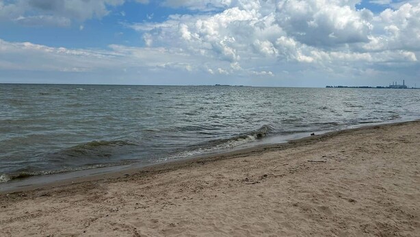 Una playa con arena y mar tranquilo bajo un cielo parcialmente nublado.