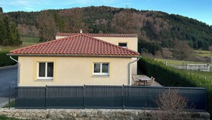 Uma casa de dois andares com telhado de telhas vermelhas, um muro de pedra e um gramado.