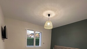 Quarto com cama, janela, televisão e luminária pendente.