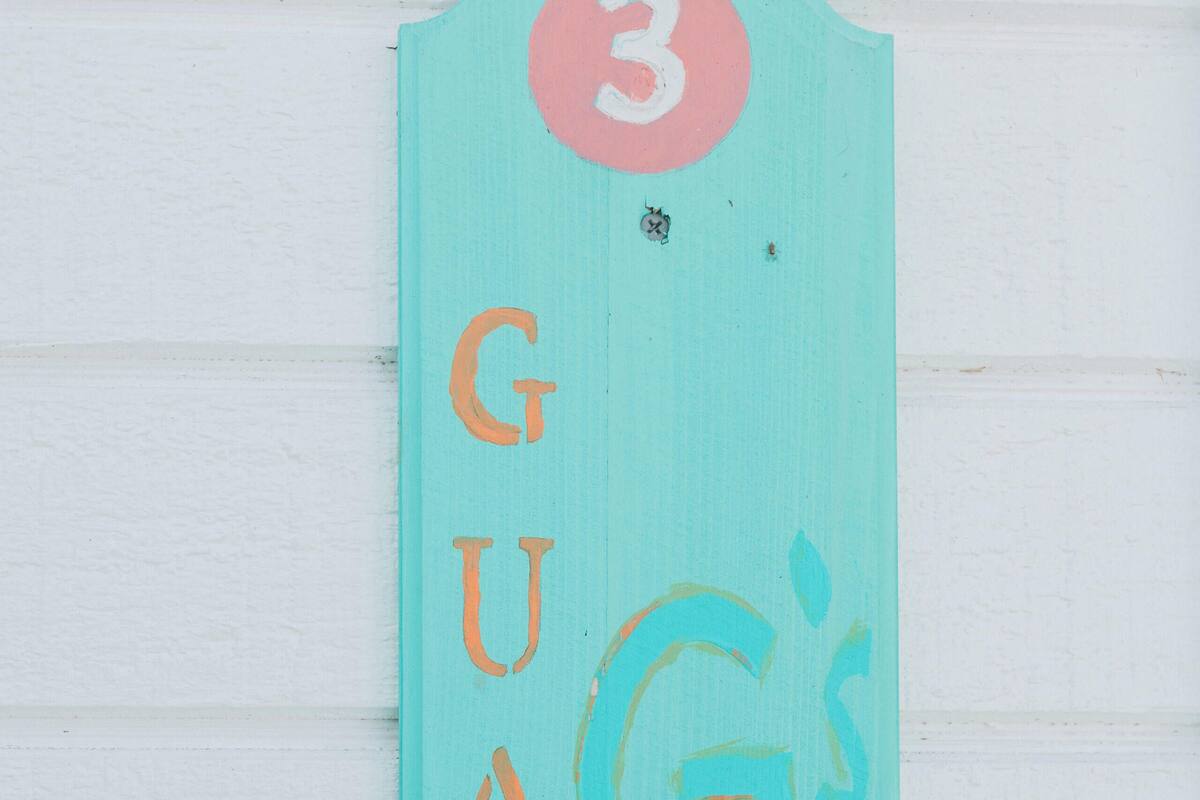 A teal sign with the number 3 and the word "GUANA" in orange letters, mounted on a white wall.