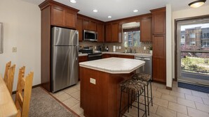 A modern kitchen with wooden cabinets, stainless steel appliances, and a large island with stools. - Winter Park Condo w/ Fireplace, Centrally Located (Winter Park)