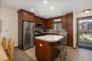 A modern kitchen with wooden cabinets, stainless steel appliances, and a large island with stools. - Winter Park Condo w/ Fireplace, Centrally Located (Winter Park)