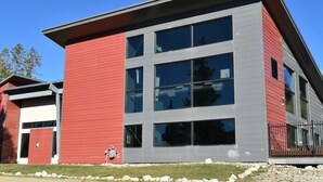 A modern building with a red and grey facade, large windows, and a metal fence. - Winter Park Condo w/ Fireplace, Centrally Located (Winter Park)
