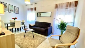 Un salon comprenant un canapé, une table basse, une table à manger avec des chaises et une plante en pot.