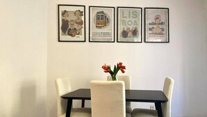 Un coin repas avec une table et des chaises, un vase rempli de fleurs et quatre affiches encadrées accrochées au mur.