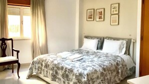 Une chambre à coucher avec un lit, une chaise, une fenêtre avec des rideaux et un luminaire au plafond.