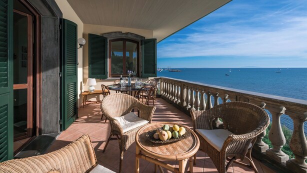 En balkon med fletningsmøbler, et bord med frugt og havudsigt.