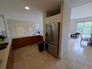 A modern kitchen with a stainless steel refrigerator, wooden cabinets, and a large window providing natural light. - Luxury Near the Sea Buenaventura | Beach, Pool, Golf and Resort Life in Río Hato (Buenaventura)