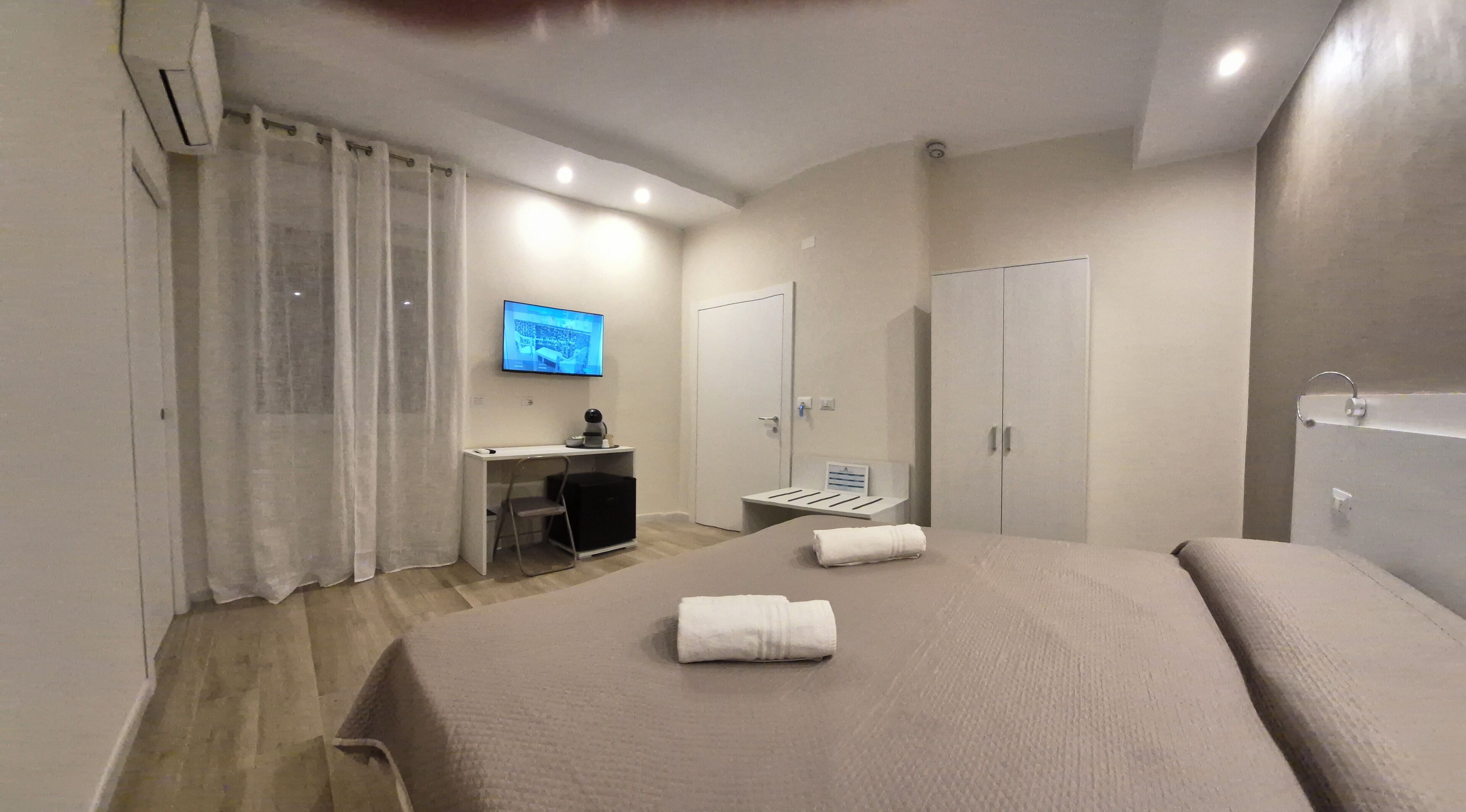Una habitación de hotel con cama, escritorio con silla, televisor, armario y baño.