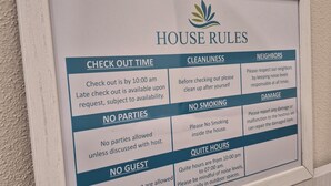A framed house rules sign with sections on check-out time, cleanliness, neighbors, no parties, no smoking, no guests, and quiet hours.