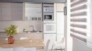 A modern kitchen with white cabinets, a built-in oven, microwave, and dishwasher. There is a dining table with chairs and a vase of flowers. - Cool Vialia (Vigo)