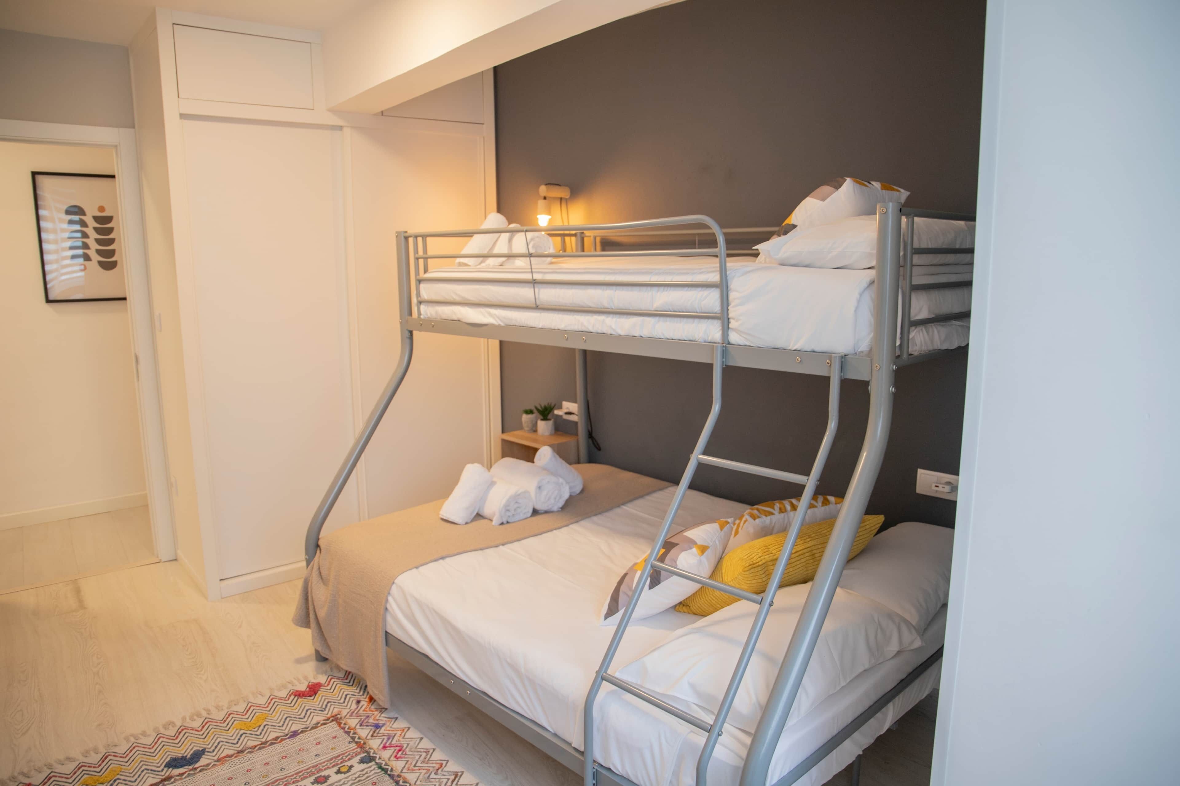 A bunk bed room with a small bedside table, a wall-mounted lamp, and a framed picture on the wall.