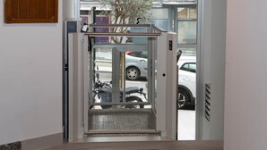 A hotel entrance with a revolving door, a metal staircase, and a view of parked cars and buildings outside. - Cool Vialia (Vigo)