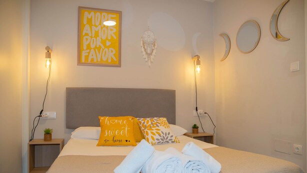 A neatly made bed with rolled white towels, a bedside table with a small plant, a wall clock, and a motivational poster. - Cool Vialia (Vigo)