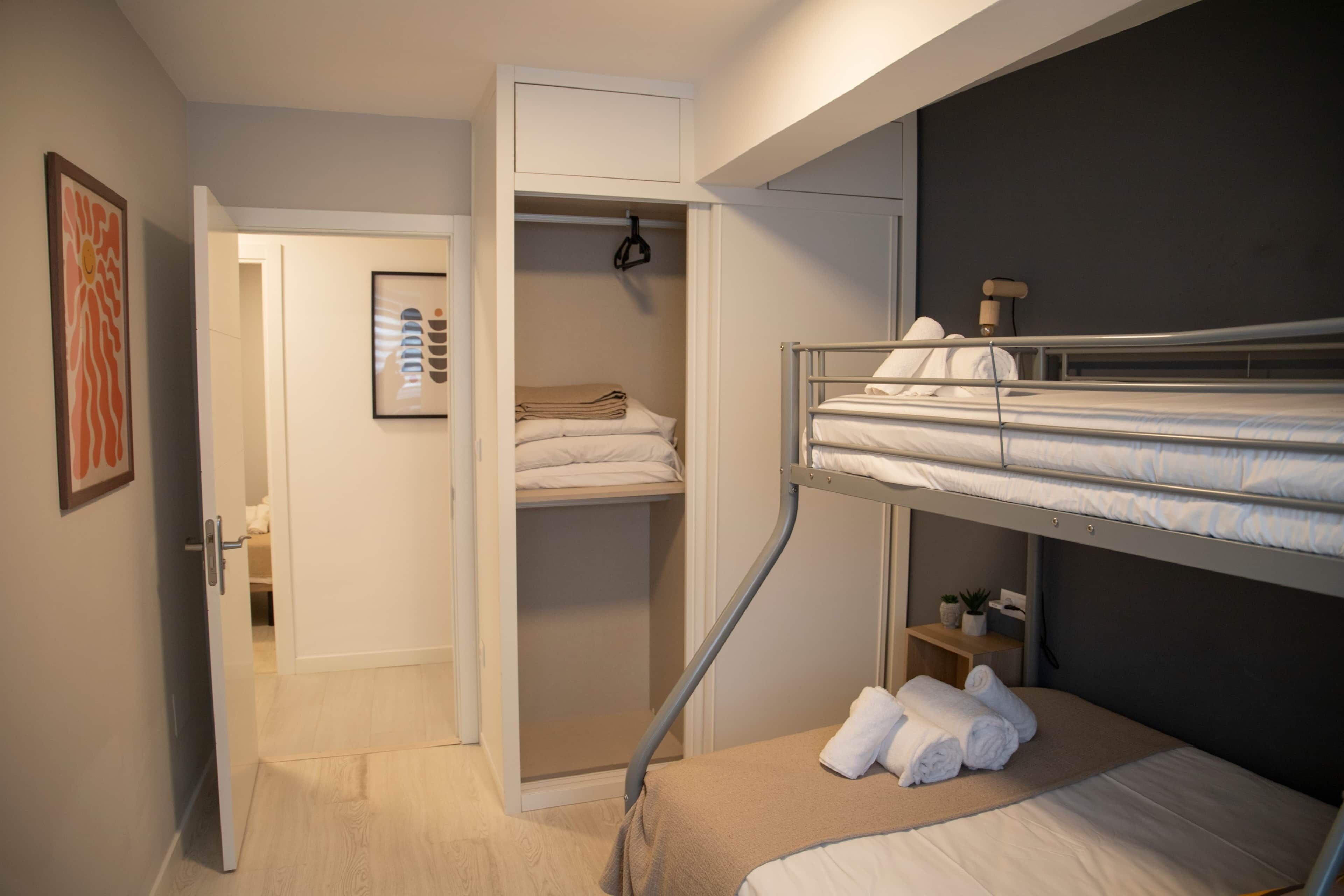 Et kompakt hotelværelse med køjeseng, et walk-in-skab og et lille sengebord med lampe.