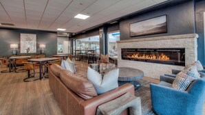 A spacious lounge area with leather seating, a fireplace, and a dining area with tables and chairs. - VIEWS! Corner Unit Next to River - Steps to Ski Slopes & Downtown Festivities (Breckenridge)