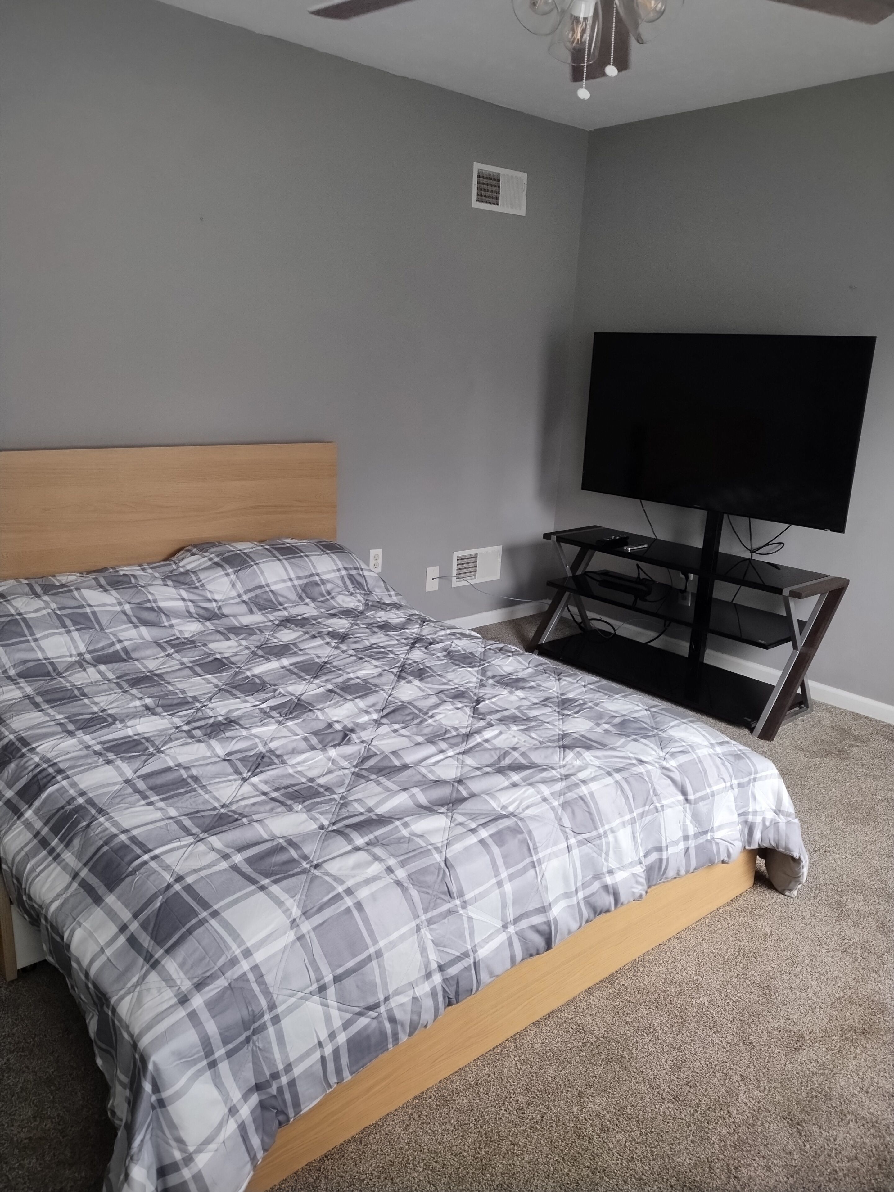 Un dormitorio con cama, televisor sobre un mueble bajo y ventilador de techo.