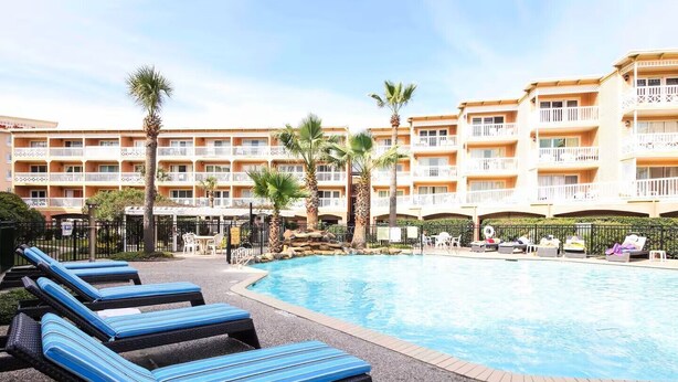 Et hotelområde med pool, liggestole og en bygning med flere etager og balkoner.