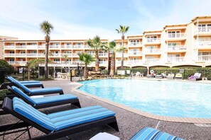 Un espace piscine d’hôtel comprenant des chaises longues, une piscine à eau claire et un immeuble à plusieurs étages doté de balcons.