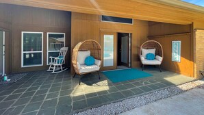 A modern building with a covered patio area featuring two wicker chairs with blue cushions, a small table, and a blue mat. - Pet-friendly 4-bedroom + Pool (Richardson)
