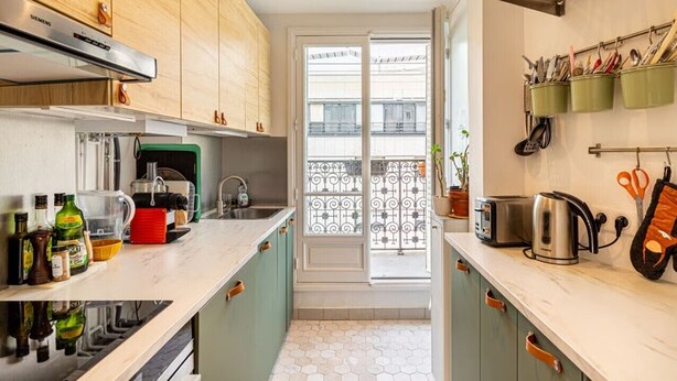 Een compacte keuken met een ingebouwde oven, een koffieapparaat en een broodrooster. Er is een raam met uitzicht op een balkon.