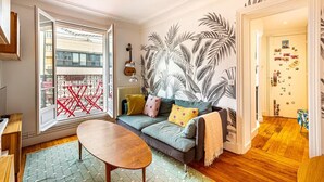 Een gezellige woonkamer met een bank, een bijzettafeltje en een groot raam met uitzicht op gebouwen.