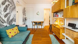 Een gezellige woonkamer met een groene bank, een houten eettafel met stoelen, en een keuken met houten kastjes en een televisie.