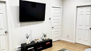 Een moderne woonkamer met een flatscreen televisie aan de wand, een zwarte mediakast en een grijze leren bank.