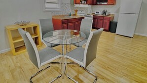 Een moderne keuken met houten kastjes, een witte koelkast en een eethoek met een glazen tafel en stoelen.