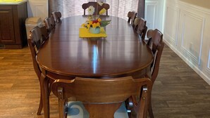 Een eetkamer met een houten tafel en stoelen, een vaas met bloemen, en een keuken op de achtergrond.