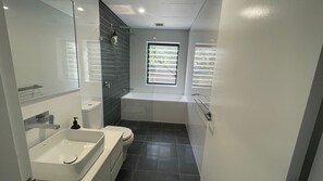 A modern bathroom with a bathtub, toilet, and sink. - Charming 2-Bedroom Unit with Stunning Back Creek Views (South West Rocks)