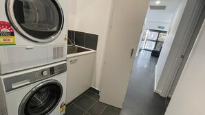 Ein Waschraum mit nebeneinander gestapelten Waschmaschinen und Trocknern, einem Waschbecken und einem gefliesten Boden.