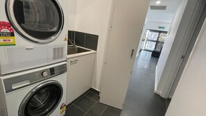 Ein Waschraum mit nebeneinander gestapelten Waschmaschinen und Trocknern, einem Waschbecken und einem gefliesten Boden.