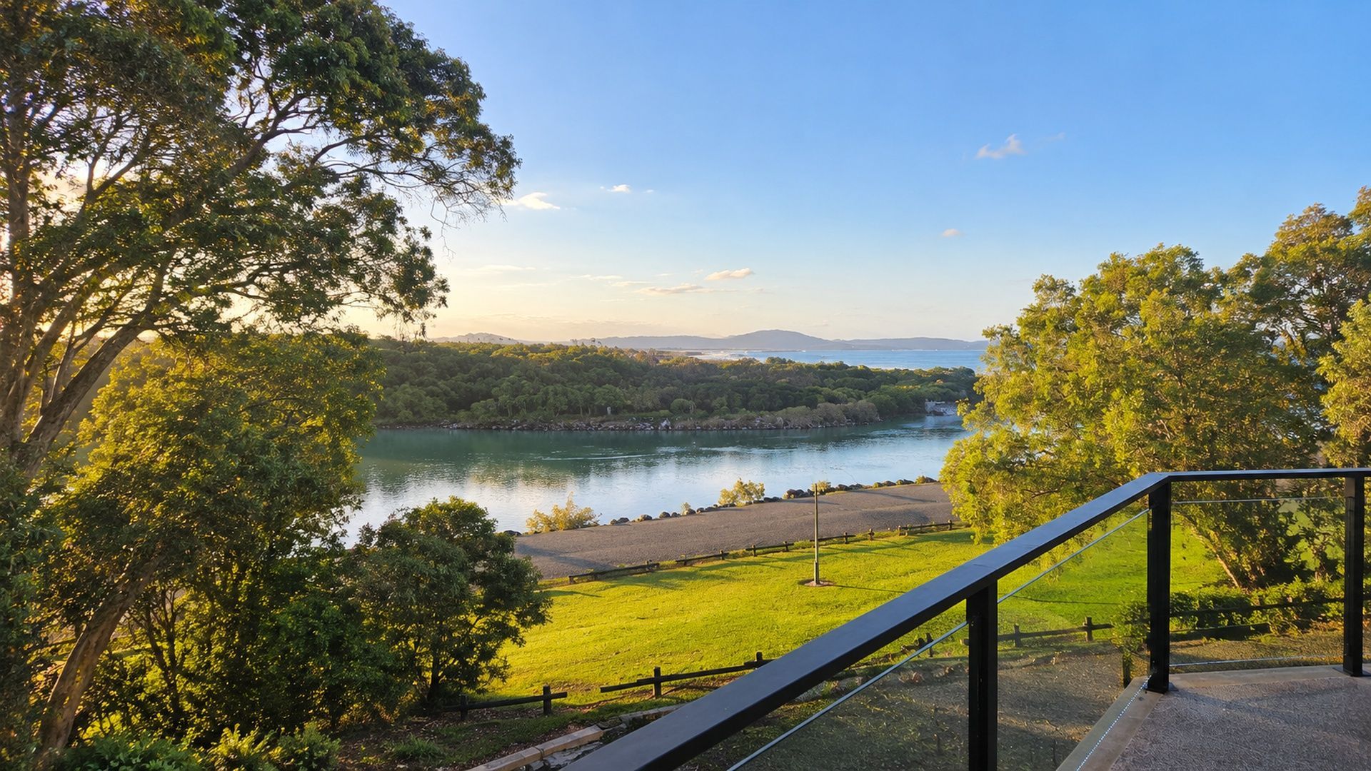 A scenic view from a balcony overlooking a river, surrounded by lush greenery and a clear sky.