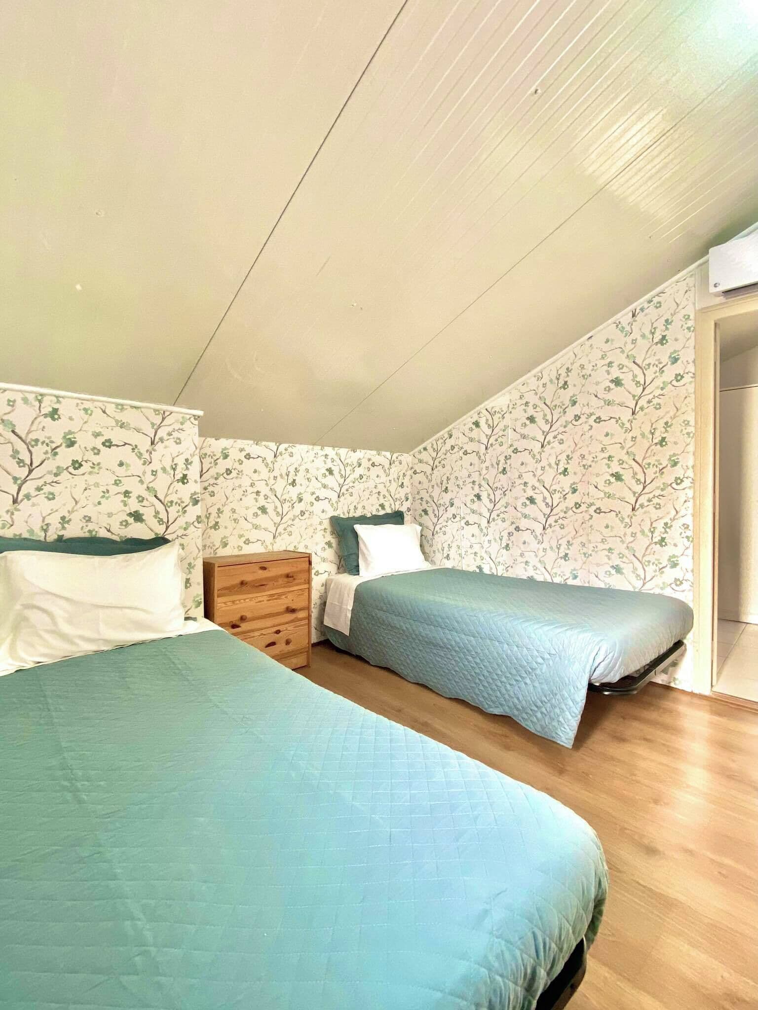 A bedroom with two beds, wooden dresser, and floral wallpaper.