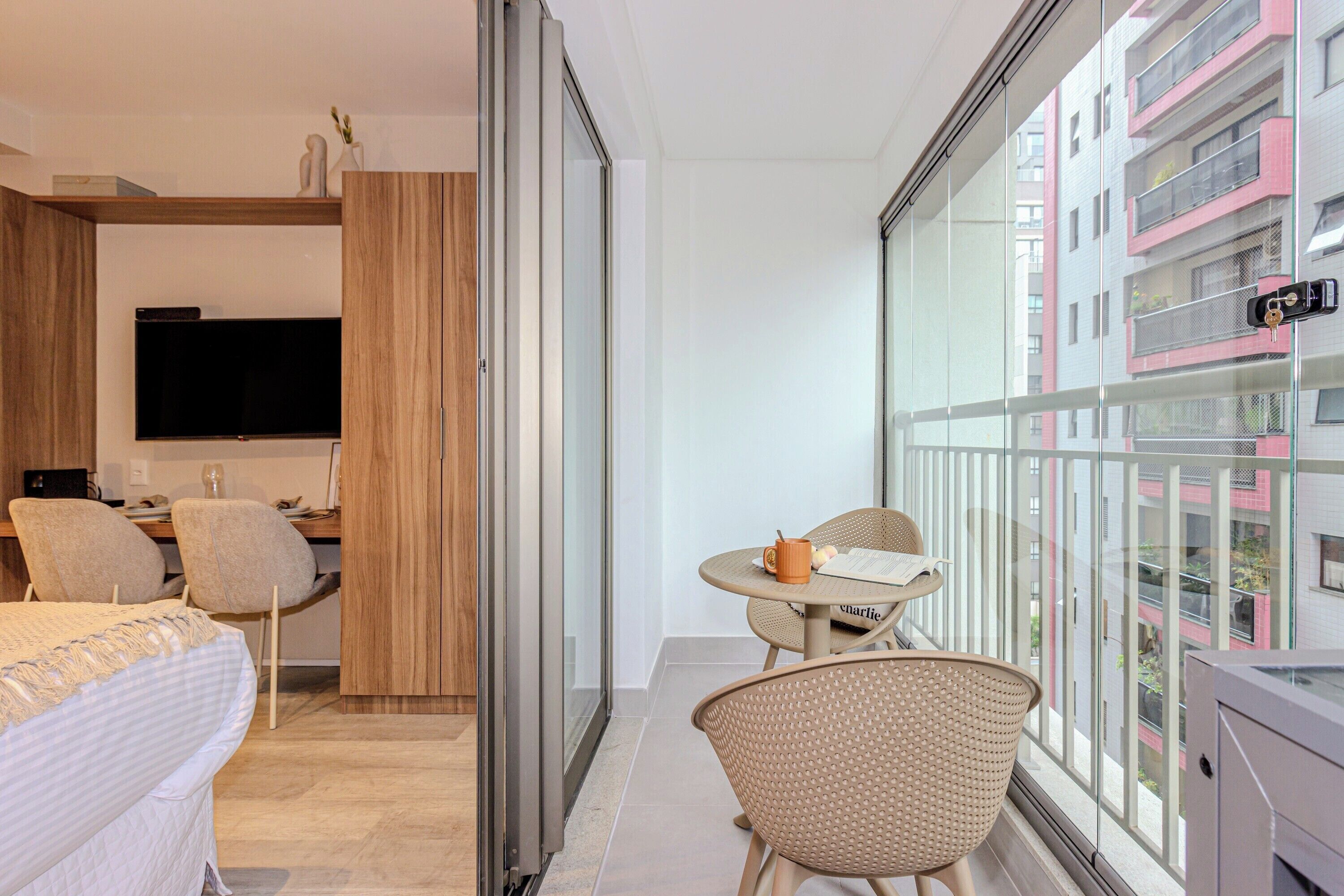 A modern hotel room with a bed, a desk, a television, and a balcony with a view of the city.