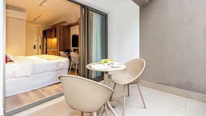 Een hotelkamer met een bed, een kleine tafel met stoel, en een glazen schuifdeur naar een badkamer.