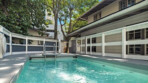 A swimming pool with a ladder, surrounded by a building with large windows and a covered deck area. - 7BD Downtown Oasis Pool  (Miami)