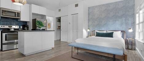 Un dormitorio moderno con una cama grande, mesitas de noche y vistas al área de la cocina.