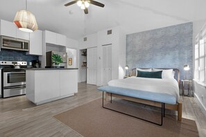 A modern bedroom with a large bed, bedside tables, and a view of the kitchen area. - 7BD Downtown Oasis Pool  (Miami)