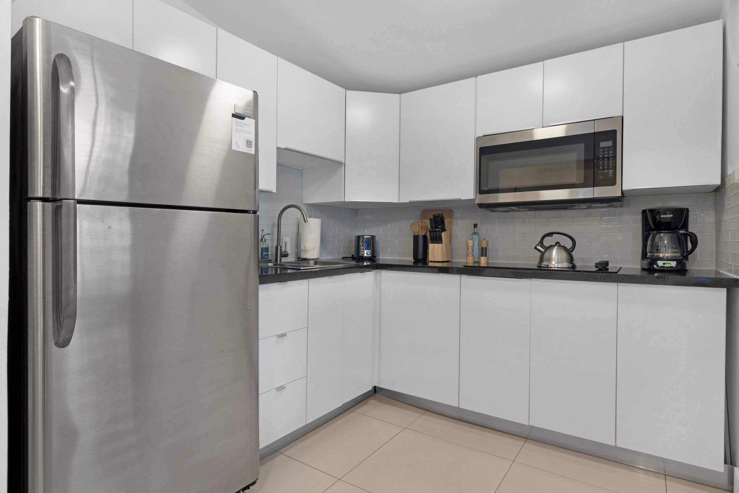 Una cocina moderna con gabinetes blancos, un refrigerador de acero inoxidable, un microondas y una cafetera.