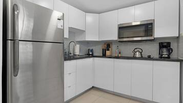 Una cocina moderna con gabinetes blancos, un refrigerador de acero inoxidable, un microondas y una cafetera.